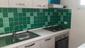 A kitchen with green tiles, a stainless steel sink, a stove, and white cabinets. - Vacation home 200 mt from the sea in sardinia (Tertenia)