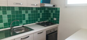 Une cuisine avec des carreaux verts, un évier en acier inoxydable, une cuisinière et des armoires blanches.