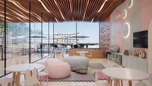 A modern indoor space with round tables, chairs, and a play area with colorful mats and a whale plush toy. - PORTO 2 LIFE RESORT (Ipojuca)