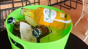 Un seau vert rempli de bouteilles de vin blanc sec Savarin, posé sur une table dans un restaurant aux murs de briques et aux chaises noires.