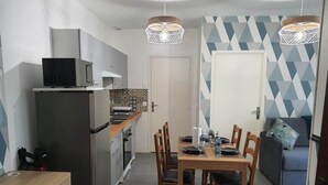 A compact kitchen with a refrigerator, microwave, and stove. There is a dining table with chairs and a sofa in the adjacent living area. - 1 Bedroom unit with balcony in front of Le Bourget Airport (Le Blanc-Mesnil)