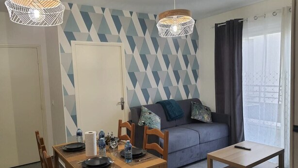 A dining area with a table set for two, a sofa, and a small table with a remote control. - 1 Bedroom unit with balcony in front of Le Bourget Airport (Le Blanc-Mesnil)