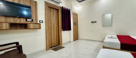 A hotel room with a flat-screen TV, wooden wardrobe, two beds, a mirror, and a ceiling fan.