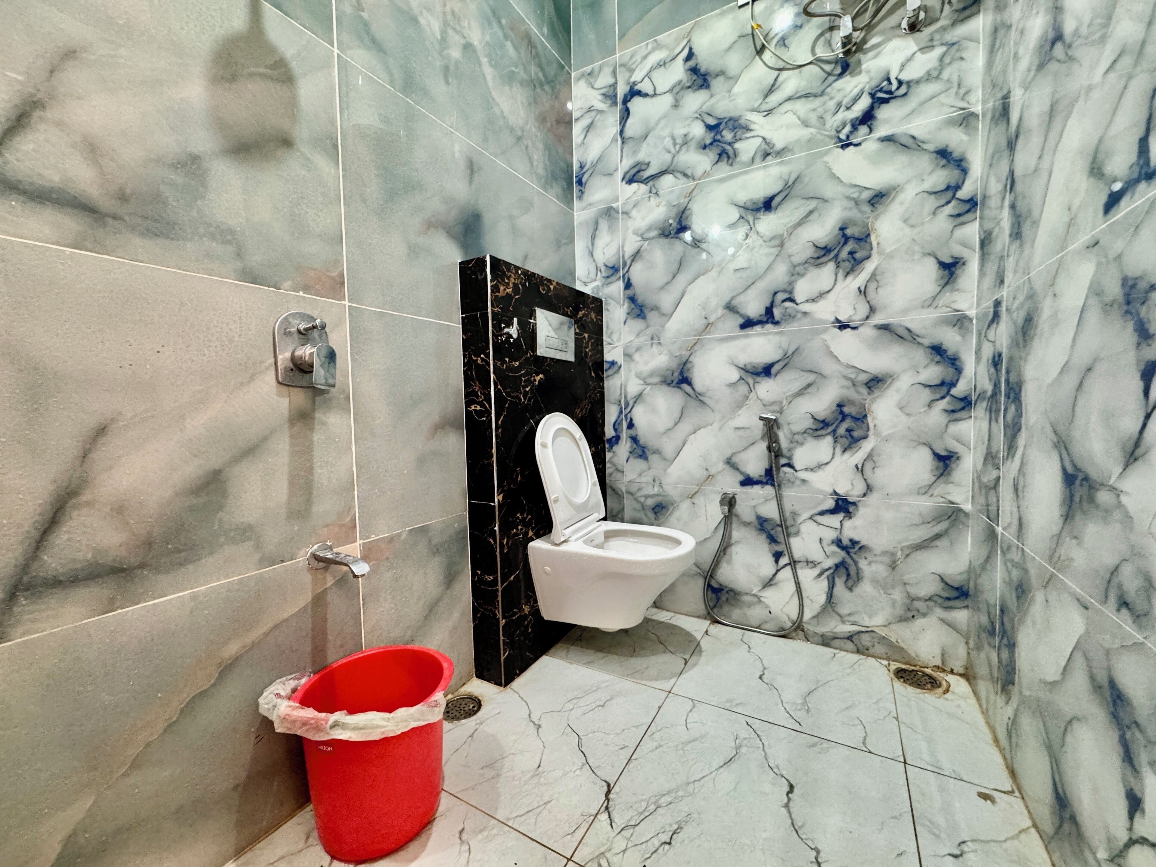 Ein Badezimmer mit Toilette, einem roten Eimer und Marmorfliesen.