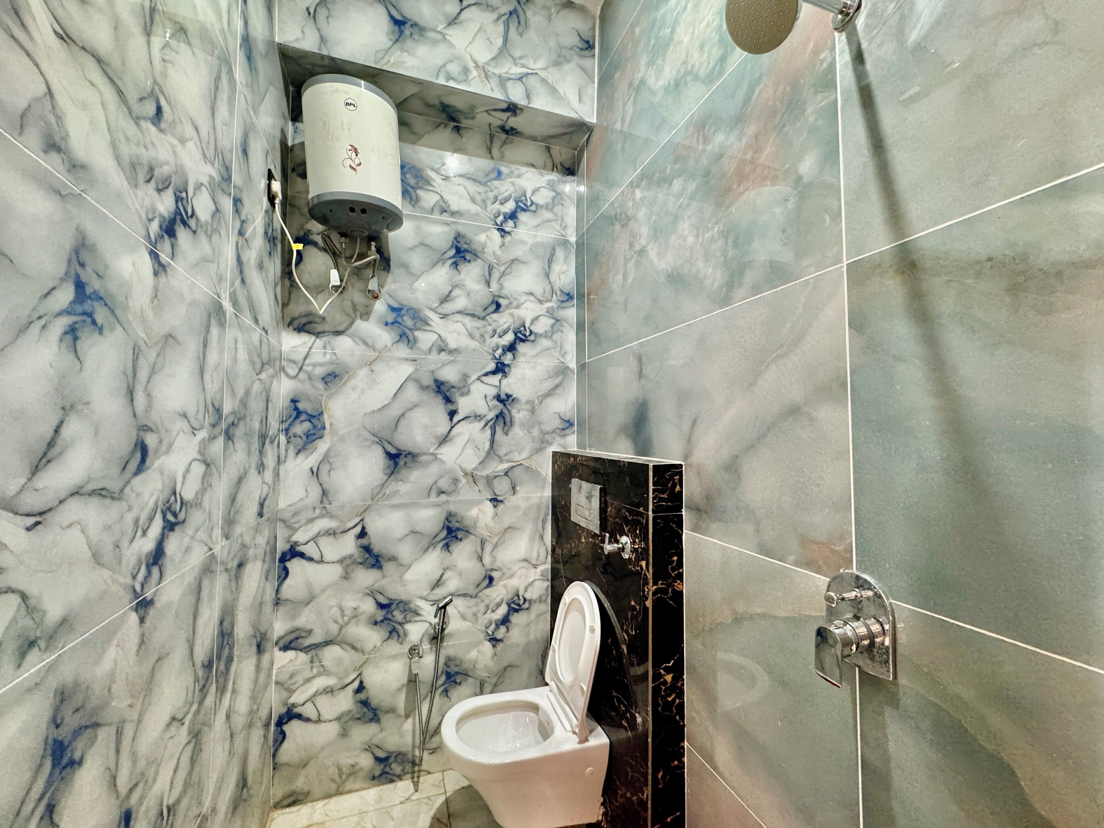 Un baño con paredes de mármol, inodoro, ducha y toallero.