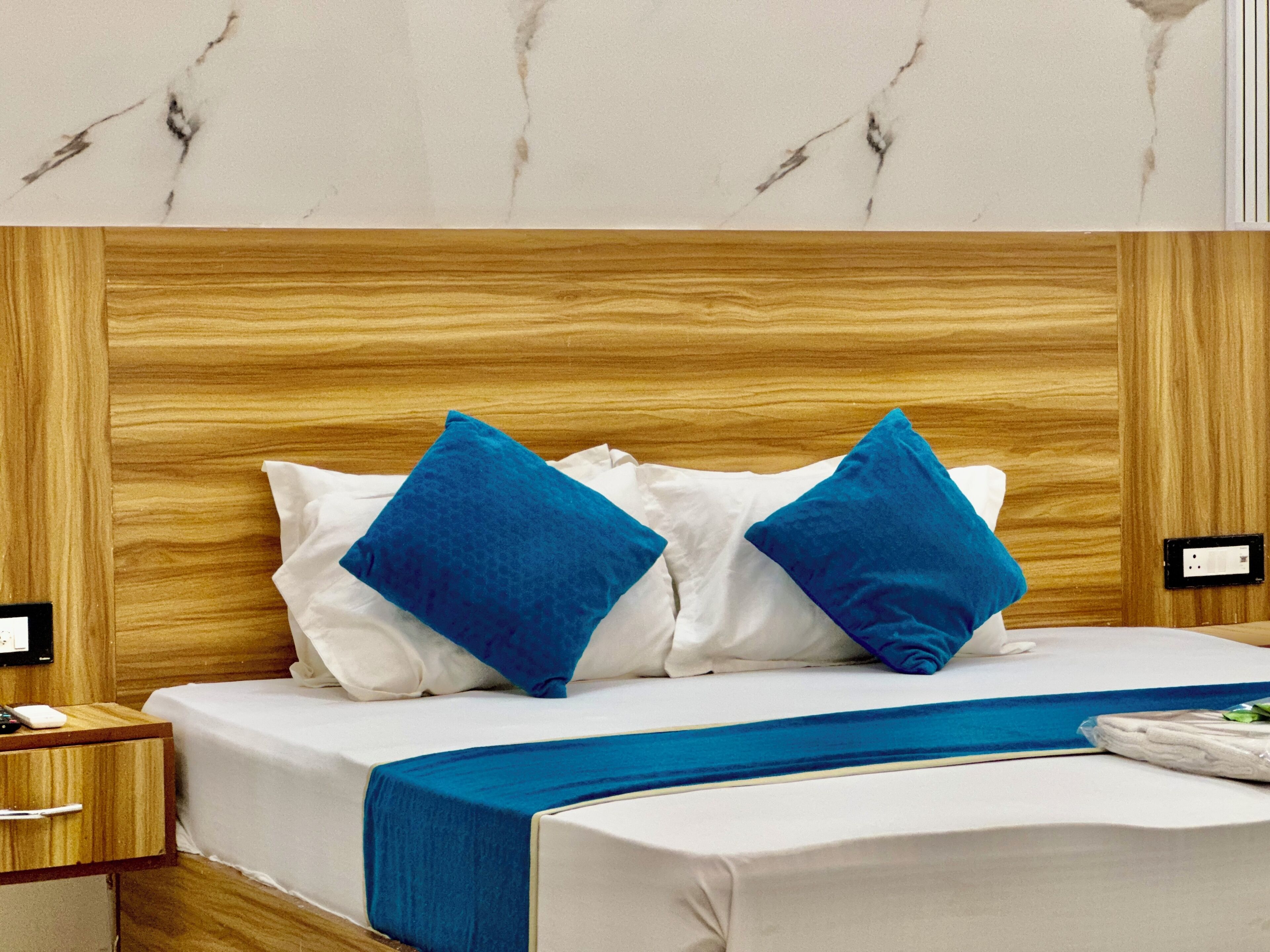 Cama bem arrumada com cabeceira de madeira, roupa de cama branca e duas almofadas azuis.