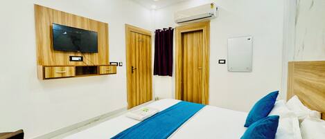 A hotel room with a bed, a TV mounted on the wall, an air conditioning unit, and wooden doors.