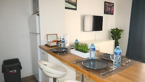 Una cucina moderna con un piano di lavoro in legno, un lavello e un frigorifero. Si vedono bottiglie d'acqua, una pianta e un televisore a schermo piatto appeso al muro.