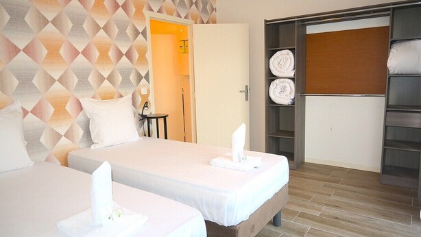 Una camera d'albergo con due letti, un armadio e un bagno visibile attraverso una porta aperta.