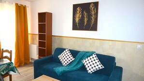 Sala de estar com um sofá azul, almofadas estampadas, manta verde-água e um quadro pendurado na parede com penas.