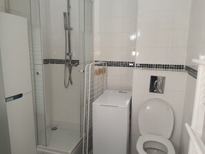 Ein kleines Badezimmer mit einer Duschkabine, einer weißen Waschmaschine und einer Toilette.
