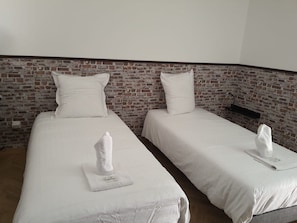 Zwei Einzelbetten mit weißen Bettwäsche und Kissen, eine Backsteinwand und ein Holzboden.