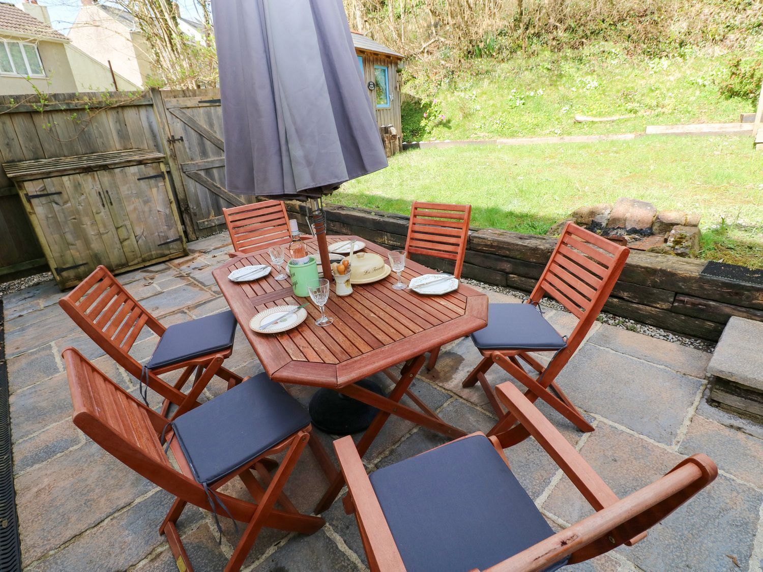 A wooden patio table set with plates, glasses, and a candle holder.