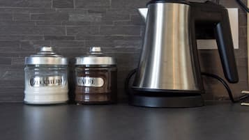 Un comptoir de cuisine avec une machine à café, deux bocaux étiquetés « ZUCCHERO » et « CAFFÈ », et un mur en briques en arrière-plan.
