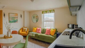 A modern living room with a green sofa, orange armchair, and a round table with a vase. - Modern Plymouth Stay- Near Barbican & City Centre- Ideal for Families / Business (Plymouth)