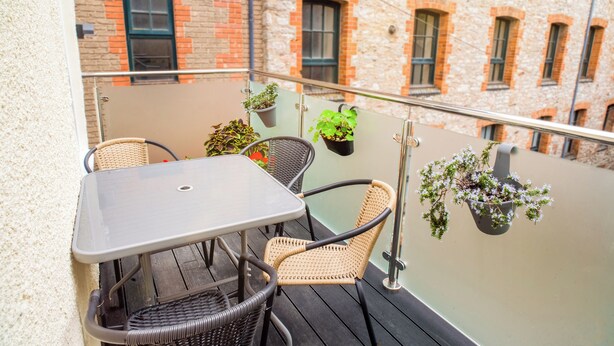 A balcony with wicker chairs, a table, and hanging planters with plants. - Modern Plymouth Stay- Near Barbican & City Centre- Ideal for Families / Business (Plymouth)