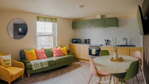 A compact living space with a sofa, a dining table, a kitchen area, and a large window. - Modern Plymouth Stay- Near Barbican & City Centre- Ideal for Families / Business (Plymouth)