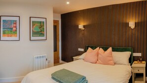 A neatly made bed with a folded towel, two framed pictures on the wall, a wooden slatted wall, and a bedside table with a lamp. - Modern Plymouth Stay- Near Barbican & City Centre- Ideal for Families / Business (Plymouth)