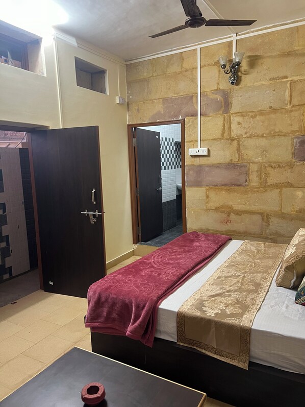 A bedroom with a bed, a ceiling fan, a door, and a small table. - La Purezza stay and restaurant (Jaisalmer)