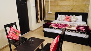 A bedroom with a bed, two chairs, a table, a ceiling fan, and a window. - La Purezza stay and restaurant  (Jaisalmer)