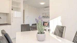 Een moderne eetruimte met een witte tafel, grijze stoelen en een pot lavendel.