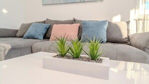 Een moderne woonkamer met een grijze bank, een witte salontafel en een kleine plantenopstelling.