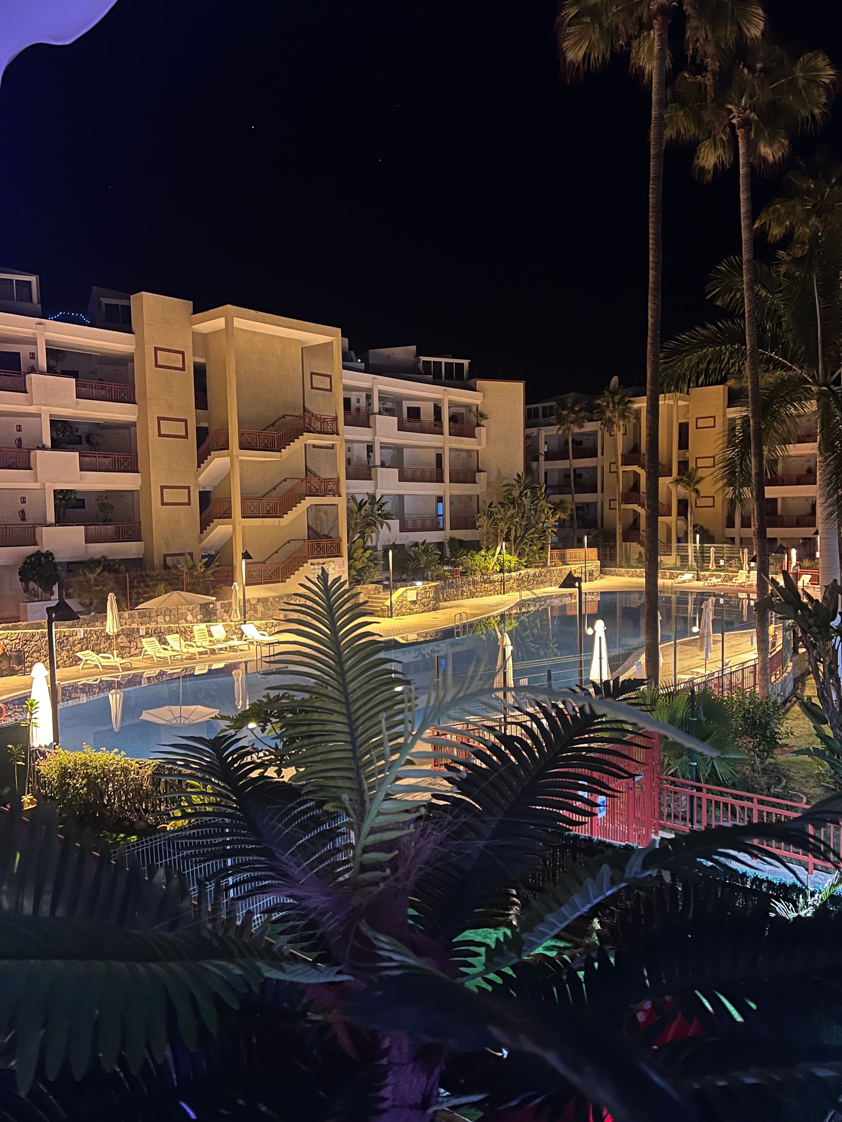 Un hotel de varios pisos con balcones, piscina y palmeras.