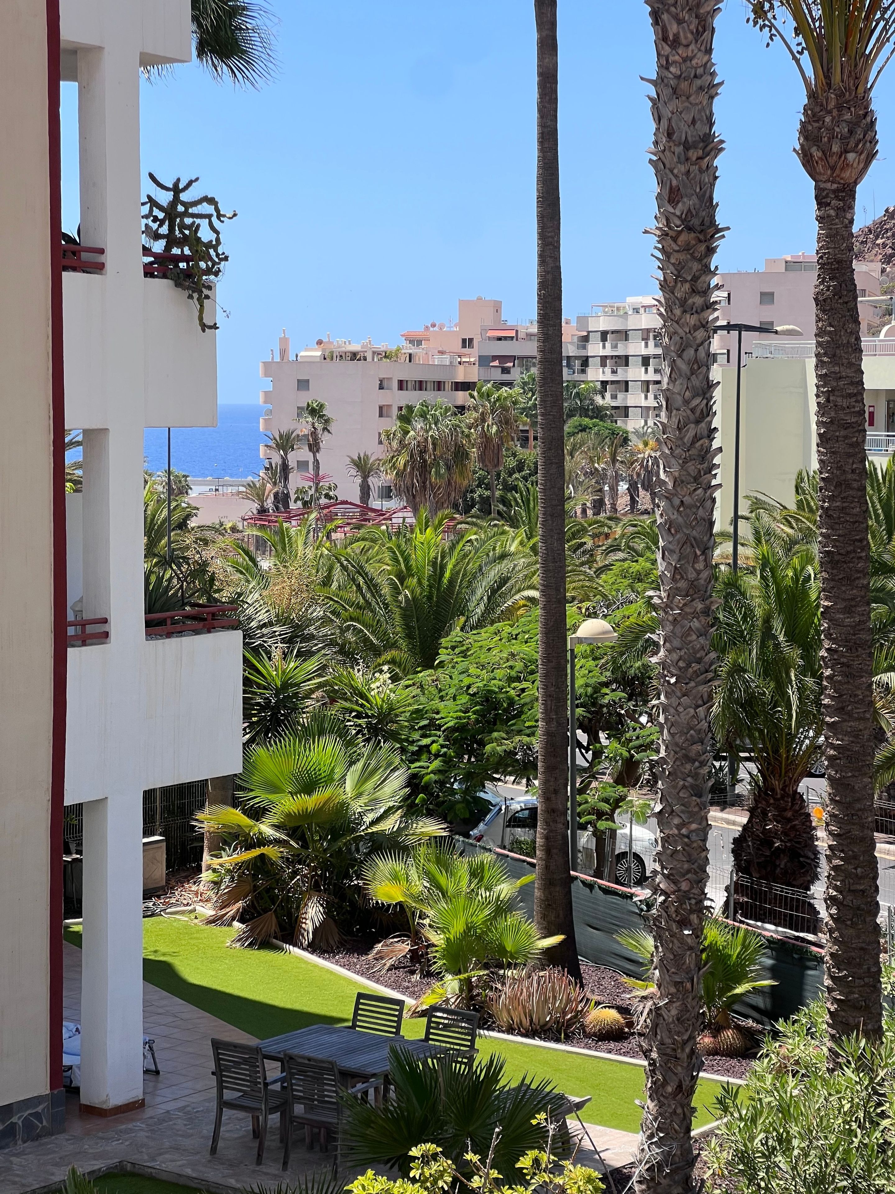 Un balcón con vistas a un jardín ajardinado, palmeras y un edificio con balcones.
