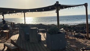 Een houten terras met buitenmeubilair, een pergola met lichtslingers en uitzicht op zee.