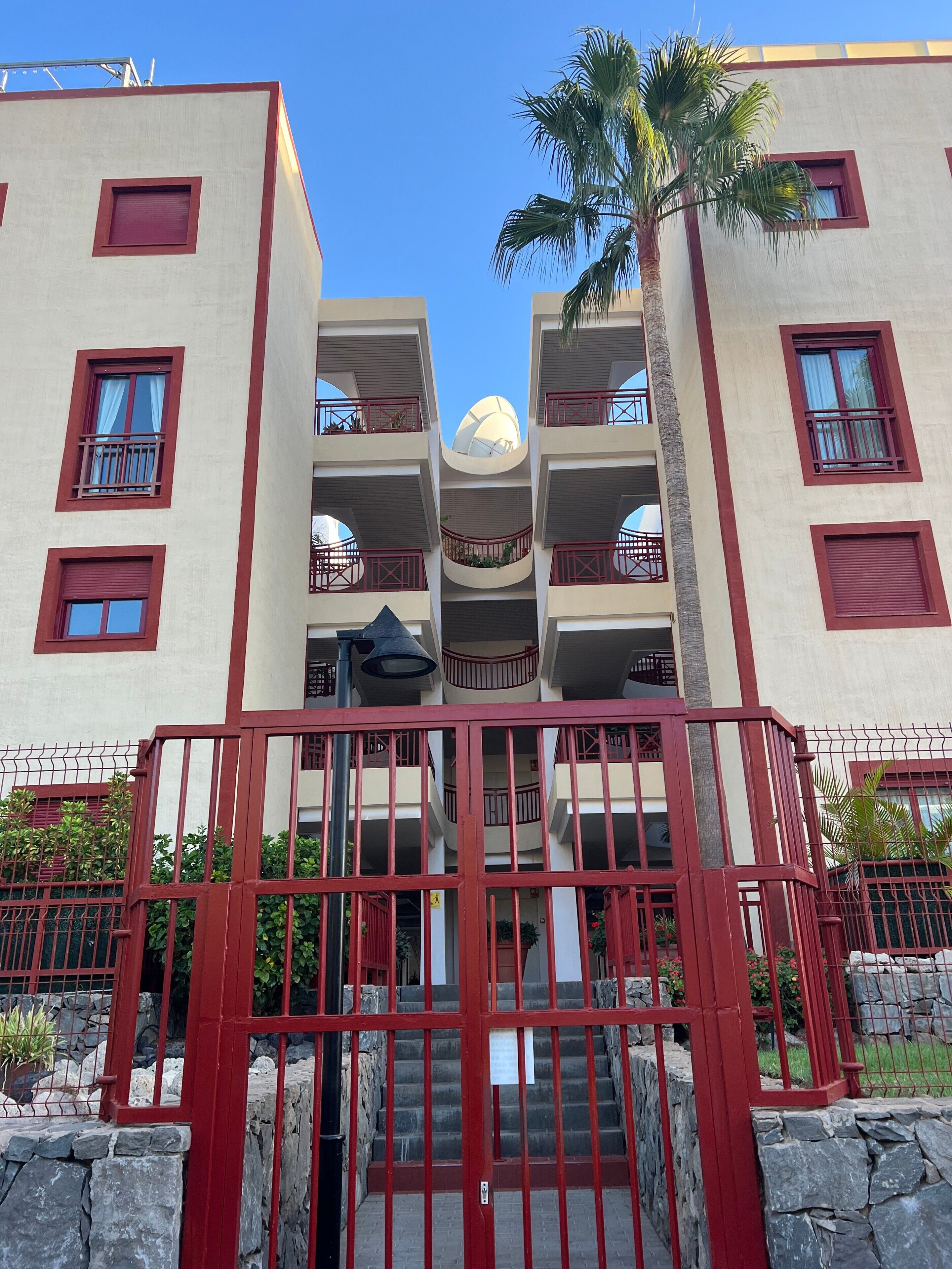 A multi-story hotel with balconies, a central dome structure, and a red gate.