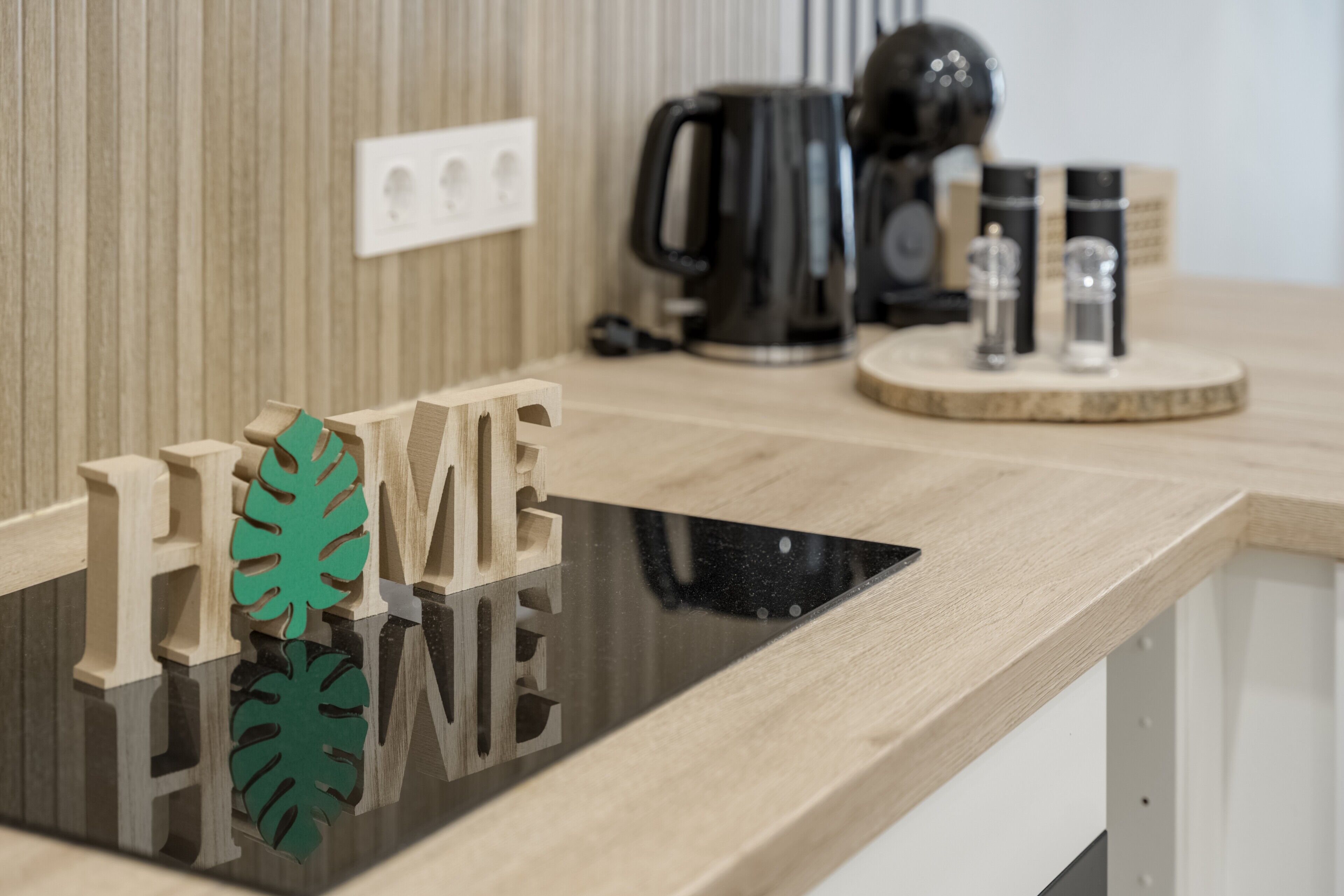 Un piano di lavoro in legno con una superficie nera riflettente, una macchina per il caffè e due coppie di posate per sale e pepe su un vassoio di legno.