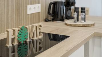 Un piano di lavoro in legno con una superficie nera riflettente, una macchina per il caffè e due coppie di posate per sale e pepe su un vassoio di legno.
