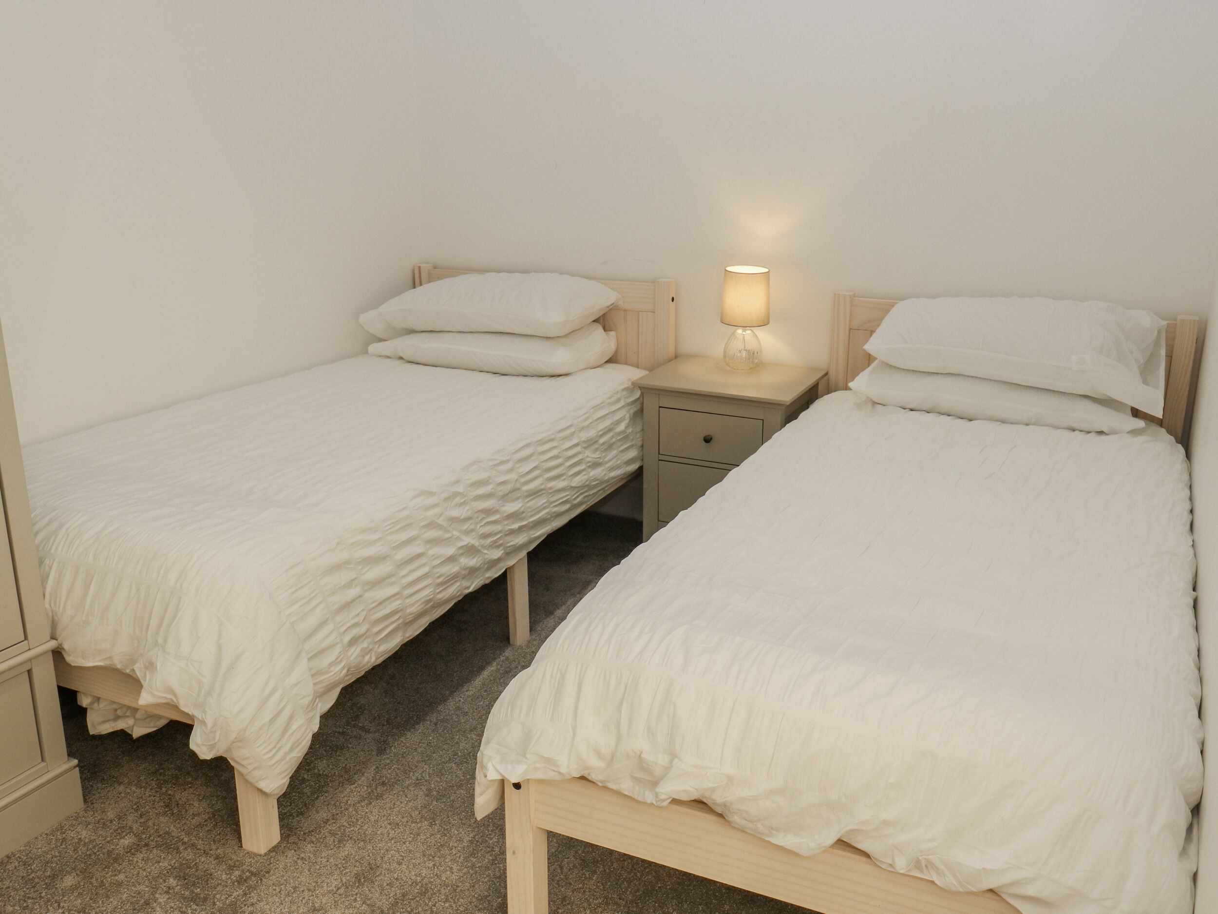 A twin room with two single beds, a bedside table with a lamp, and a small drawer.