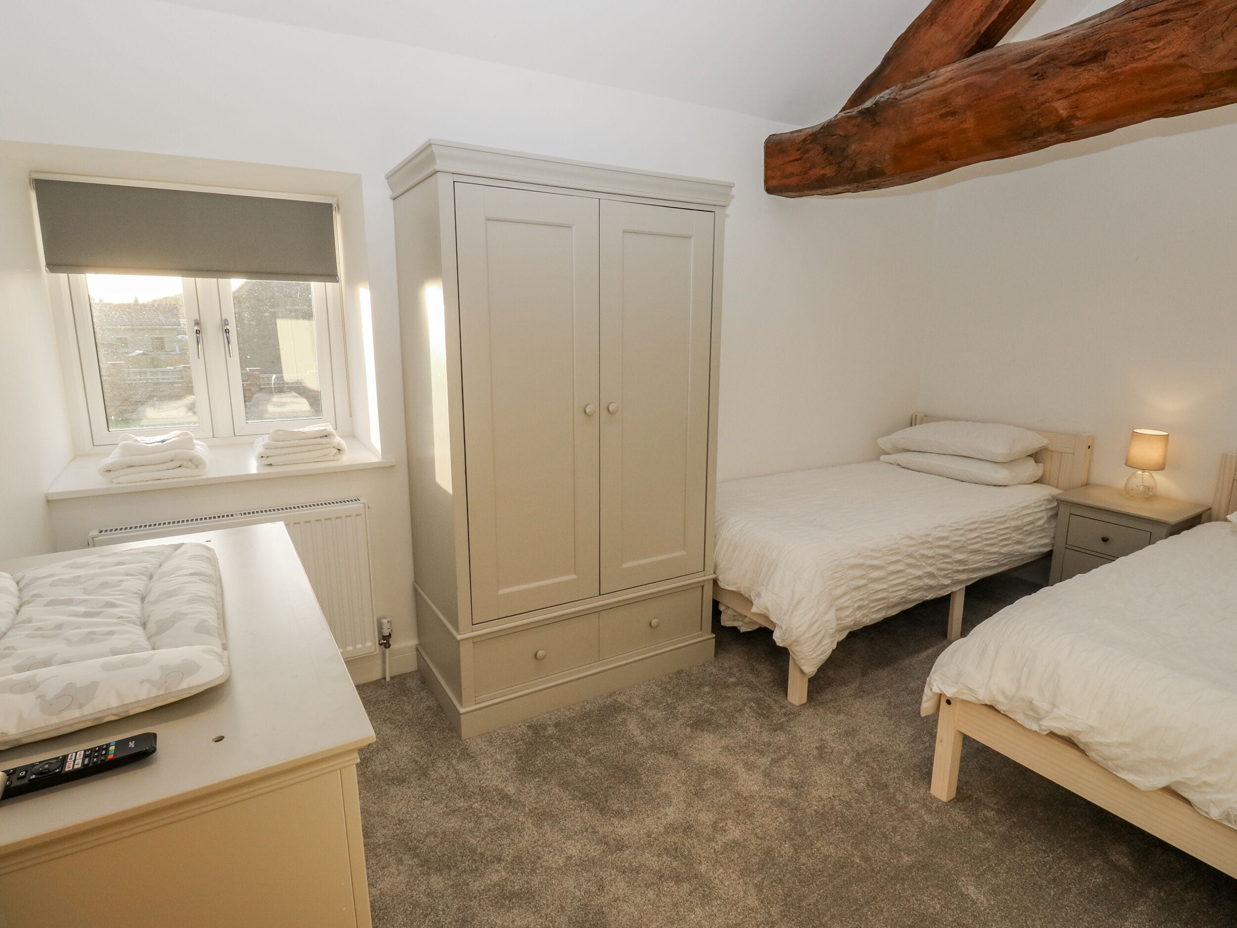 A bedroom with two single beds, a wardrobe, a radiator, and a window with blinds.