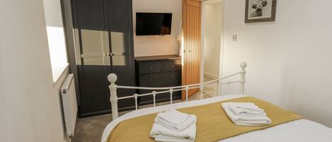 Un dormitorio con cama, armario, televisor y puerta que da a otra habitación.
