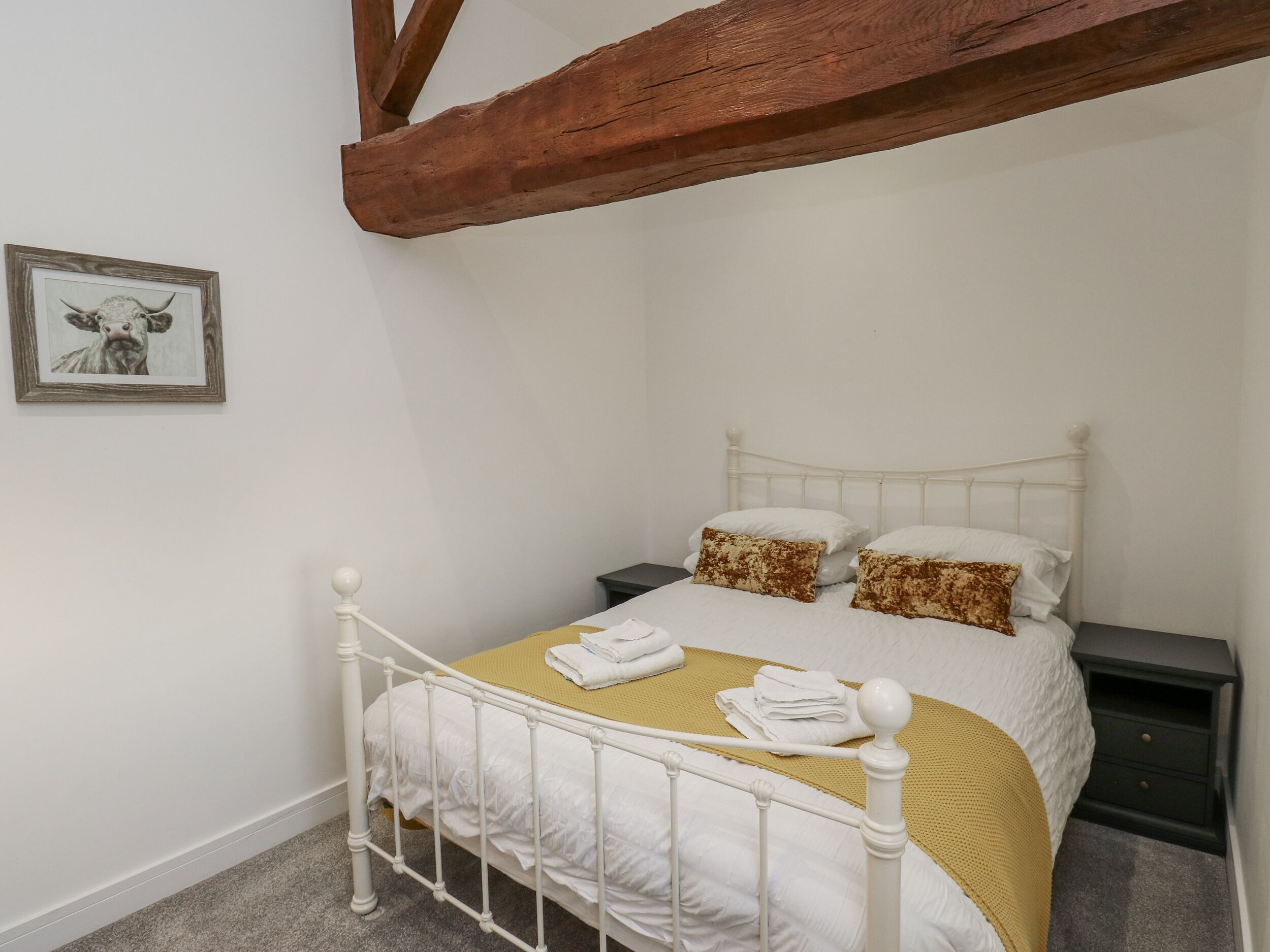 A neatly made bed with white bedding and two pillows, a wooden headboard, and a framed picture on the wall.