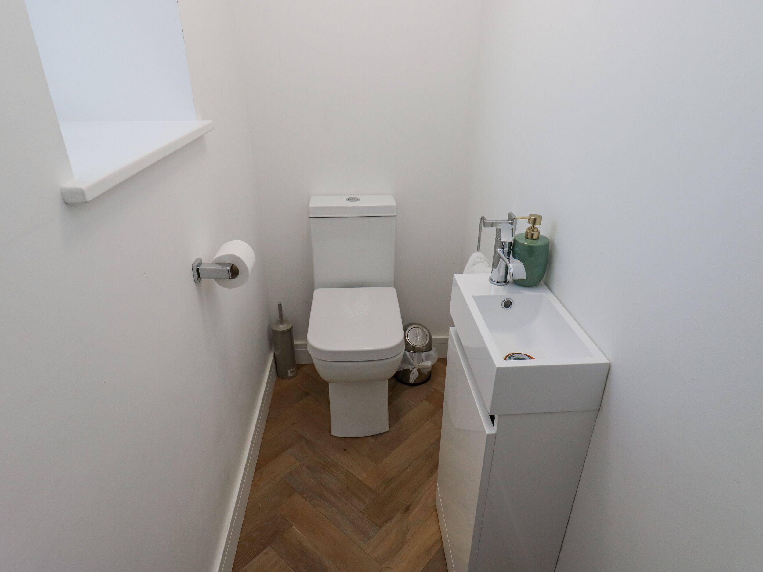 Een kleine, schone badkamer met toilet, wastafel en een raam boven het toilet.