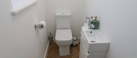 Een kleine, schone badkamer met toilet, wastafel en een raam boven het toilet.