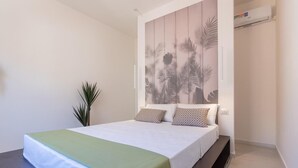 Een moderne hotelkamer met een bed, een bankje, een potplant en een wandairconditioner.