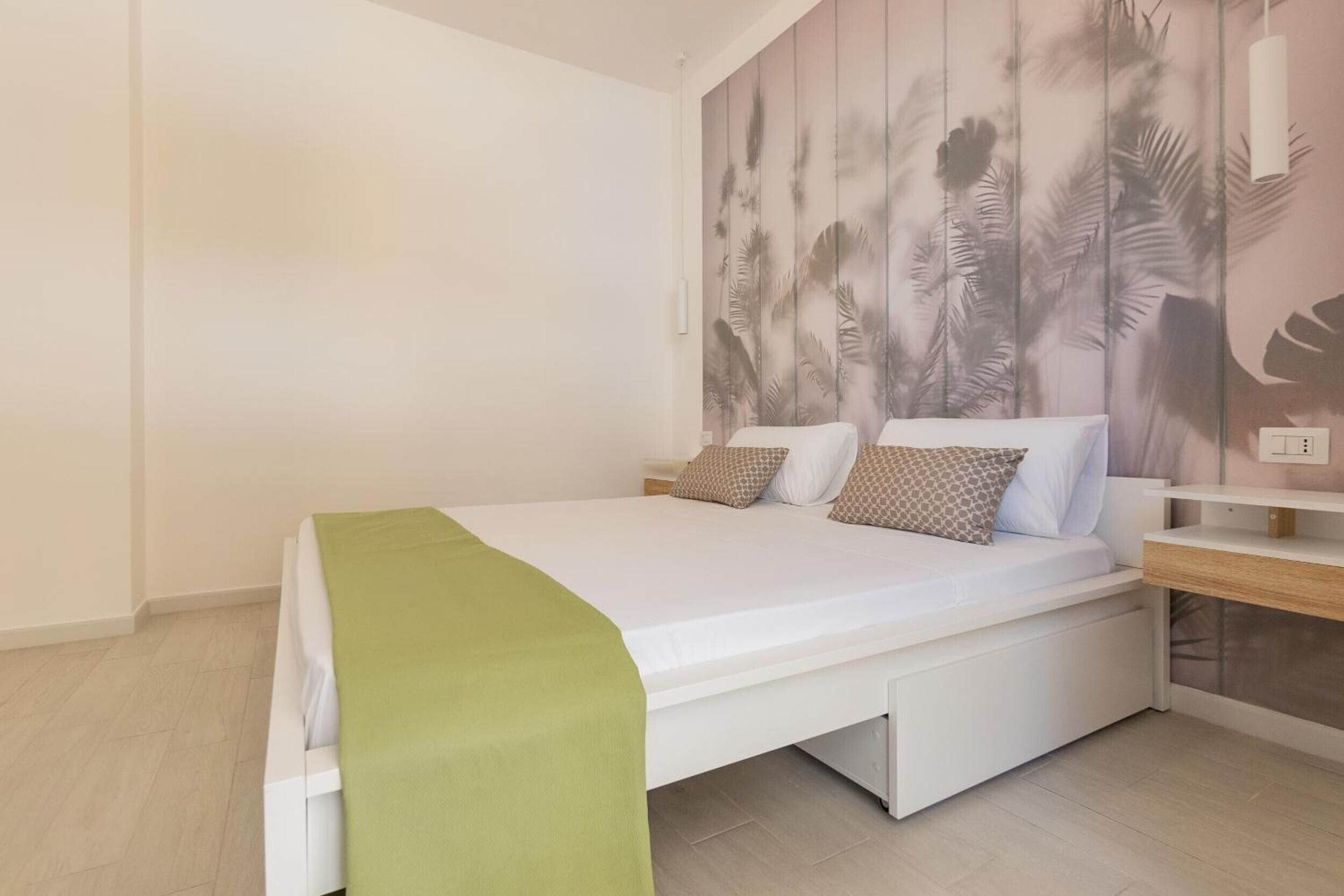 Un dormitorio moderno con una cama, una mesita de noche y una pared con un diseño de hojas.