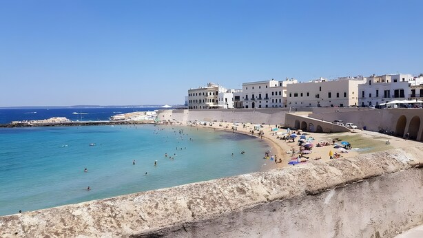 Une ville côtière dotée d’une plage, d’eaux d’un bleu limpide et de bâtiments historiques qui bordent le littoral.
