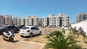A parking area with multiple cars and a few scooters, surrounded by buildings with balconies and air conditioning units.