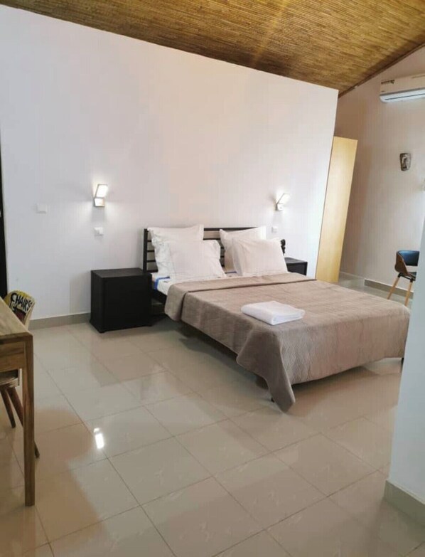 Un dormitorio con una cama, mesitas de noche, una silla y una pequeña mesa.