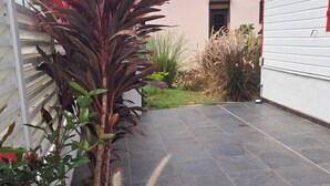 Ein gepflasterter Patio-Bereich mit verschiedenen Pflanzen, darunter eine große Pflanze mit roten Blättern und blühende Pflanzen mit roten Blüten.