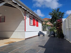 A white building with red shutters, a tiled patio, and a tree. - Spacious villa with panoramic ocean views: accommodates up to 7 guests + 2 cribs. (Ducos)