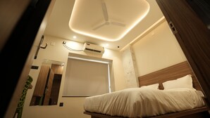 A modern hotel room with a bed, a ceiling fan, an air conditioning unit, a mirror, and a window with curtains. - AANGAN INN (Bhubaneshwar)