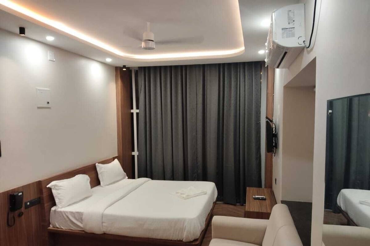 A modern hotel room with a large bed, a sofa, a bedside table, and a TV.