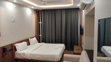 A modern hotel room with a large bed, a sofa, a bedside table, and a TV.