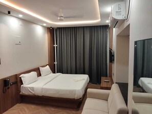 A modern hotel room with a large bed, a sofa, a bedside table, and a TV. - AANGAN INN (Bhubaneshwar)