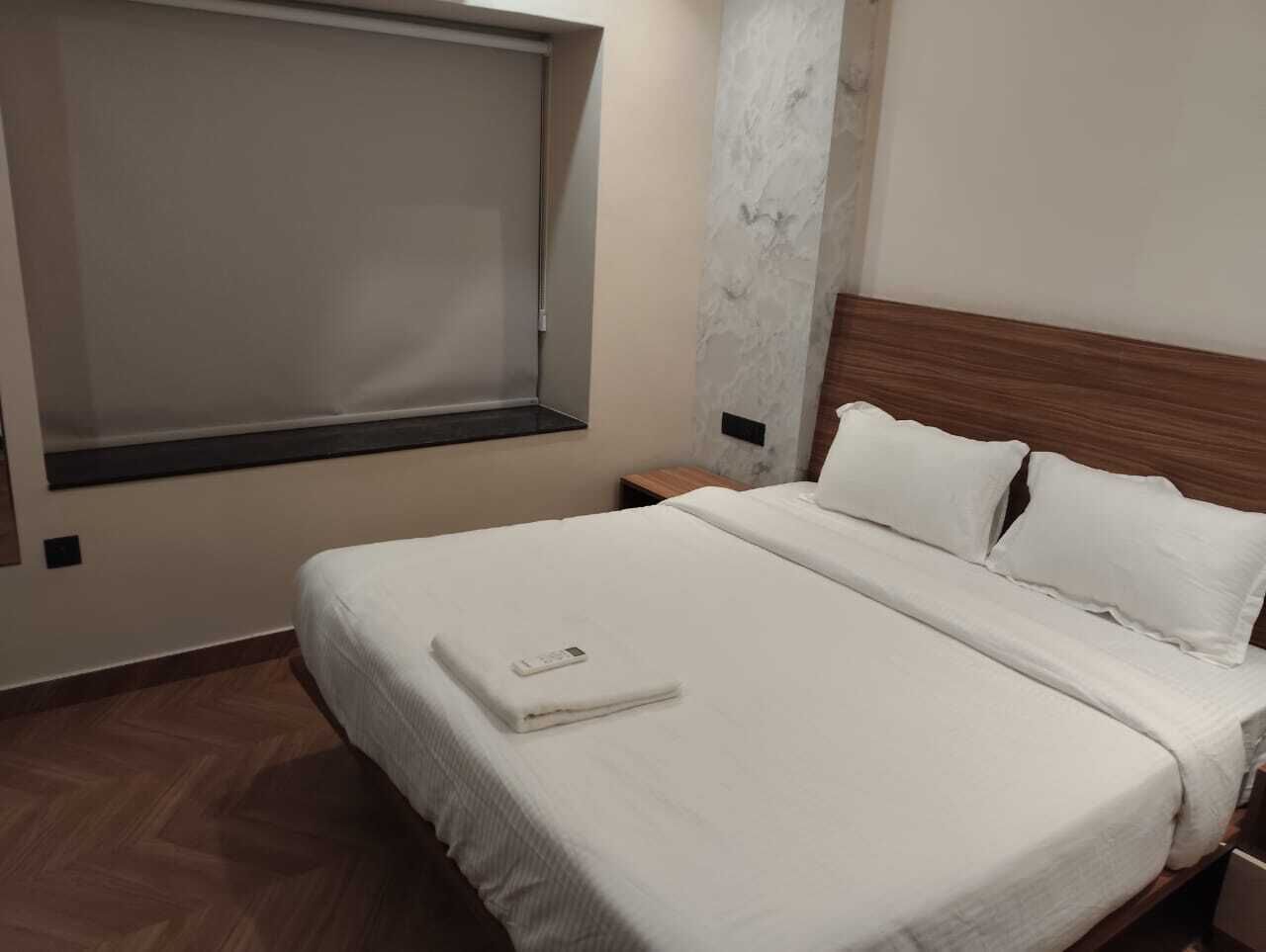 A hotel room with a bed, a nightstand, a window, and a marble wall.